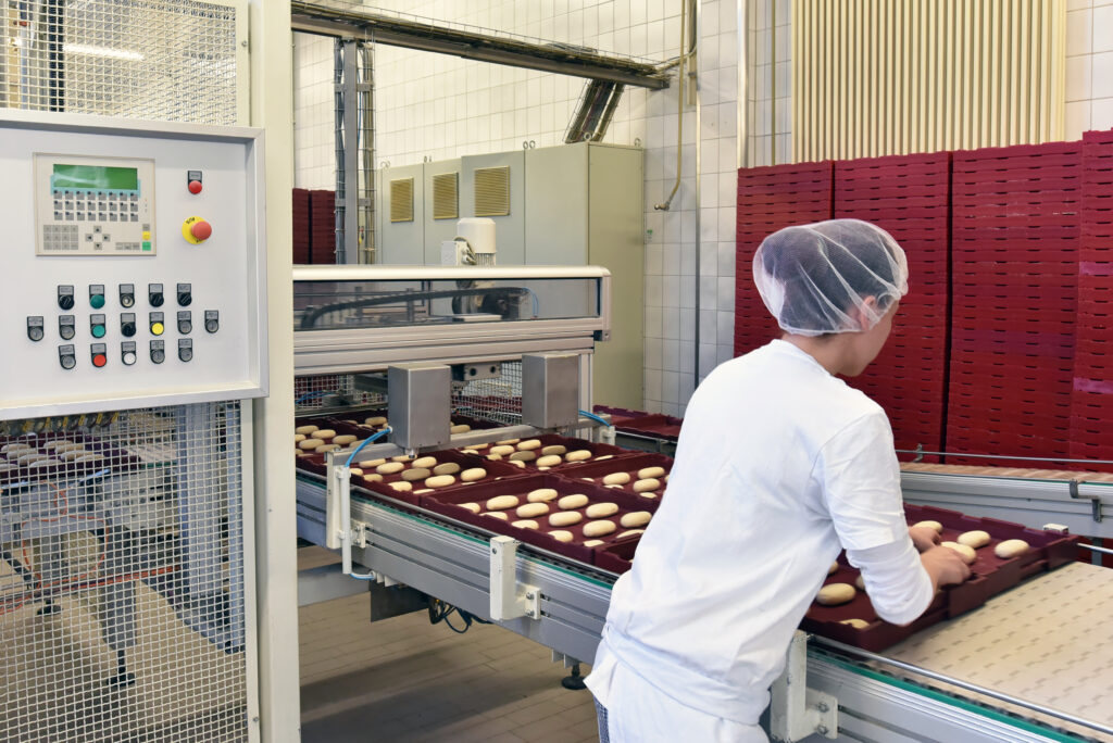Profissional de qualidade com jaleco inspecionando a linha de produção em uma indústria de alimentos para garantir a segurança de alimentos.